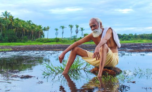 Man sitting by lake against sky