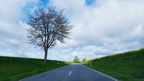 Empty road amidst fields against cloudy sky