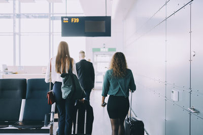 Rear view of multi-ethnic business colleagues walking with luggage by wall at airport