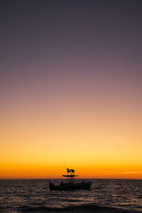 Silhouette boat in sea against clear sky during sunset