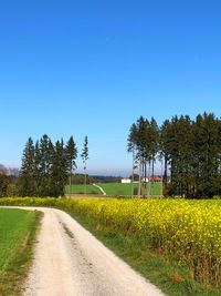 Road amidst field against clear blue sky