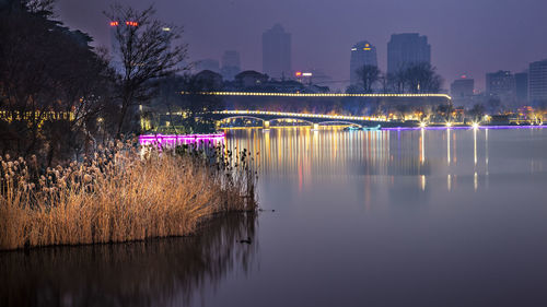 Illuminated bridge over river in city against sky at night