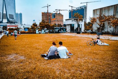 Rear view of people sitting on sidewalk in city