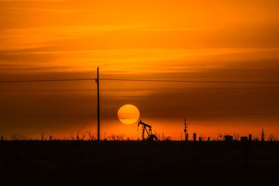 Silhouette electricity pylon on land against romantic sky at sunset