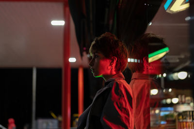 Pensive woman against glass wall on the street with red neon light at night. sad and loneliness.