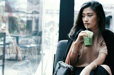 Beautiful woman drinking while looking through window at cafe