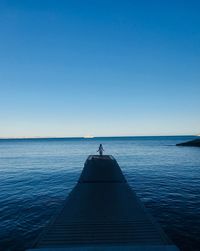 Mid distance view of woman on pier over sea against clear sky