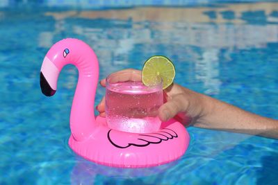Woman in swimming pool holding glass of water on a pink flamingo float 