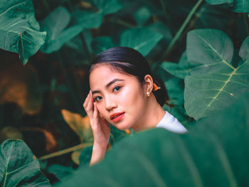 Portrait of young woman standing by plant outdoors