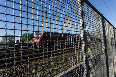 Train on railroad track seen through metallic fence against clear sky