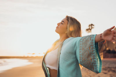 Side view of young woman standing against sky