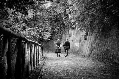 Rear view of men walking on dirt road by wall
