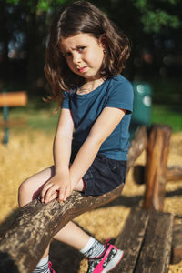 Portrait of a caucasian beautiful girl sits half-side on a wooden pole in a park