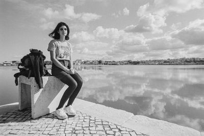 Portrait of woman sitting on pier by lake against sky