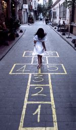 Full length of girl playing hopscotch on road in city