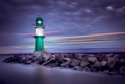 Lighthouse by sea against sky at night