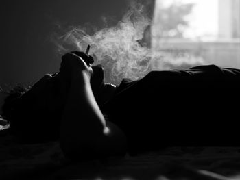 Man smoking cigarette while lying down on bed at home