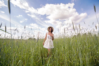 Young woman with long black hair stands in white dress and clothes straw hat is on the green field 