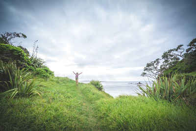 Man standing on grass by sea against sky