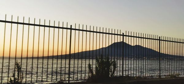 Silhouette fence by sea against clear sky during sunset