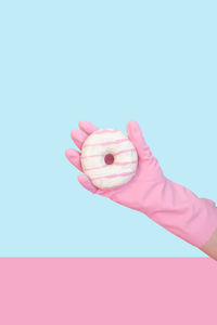 Close-up of hand holding pink umbrella against blue background