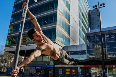 Low angle view of shirtless young man exercising against building in city