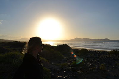 Young woman looking at sea against sky during sunset