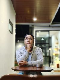 Young man looking away while sitting on table