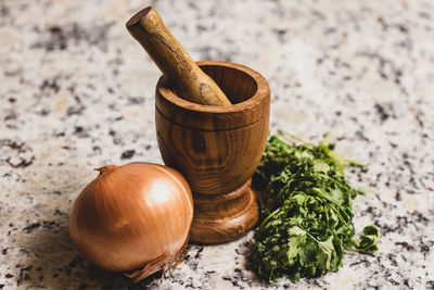 Still life image of wooden mortar and pestle, onion and cilantro.