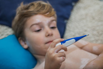 Boy infected with chickenpox holding thermometer