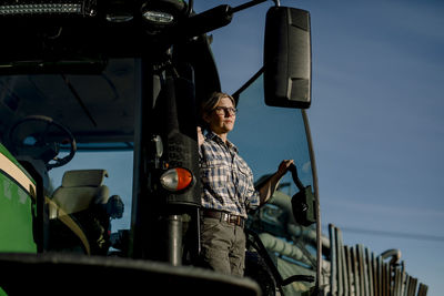 Contemplative farmer standing on tractor at farm