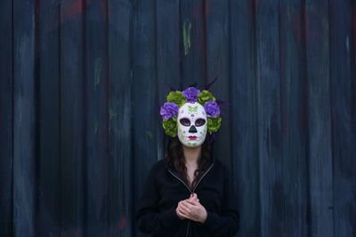 Woman wearing mask standing against wooden wall