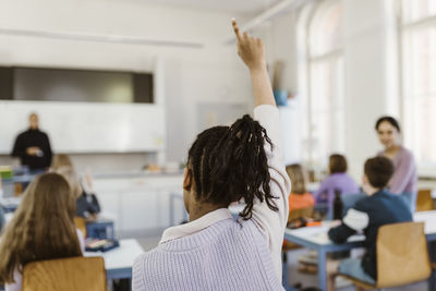 Rear view of female student raising hand during lecture in classroom
