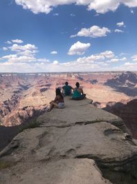 People sitting on rock against sky