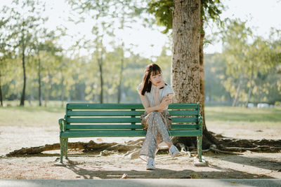 Woman listening to music while sitting on bench in park