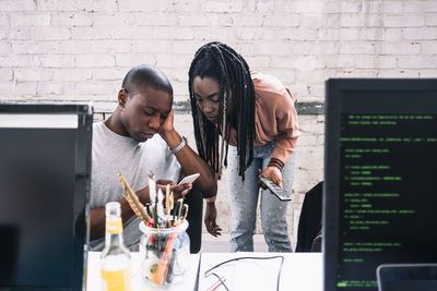 Young businesswoman looking at businessman using smart phone in creative office