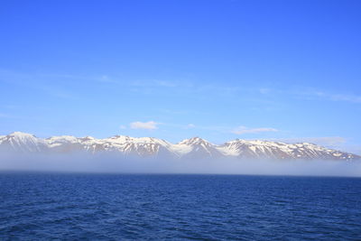 Scenic view of sea by snowcapped mountain against blue sky