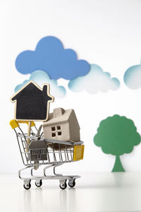 Close-up of model home in miniature shopping cart against white background