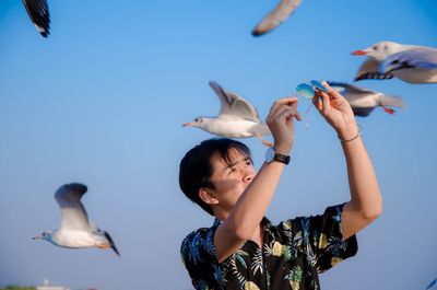 Man holding sunglasses while standing by seagulls flying against sky