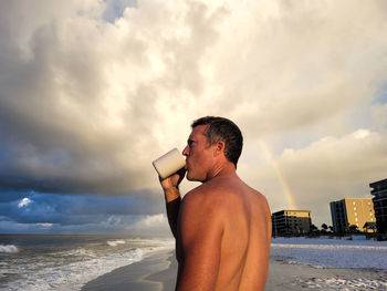 Young man gen x walking down beach to a rainbow.