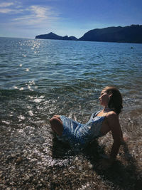 Rear view of woman sitting on rock by sea against sky