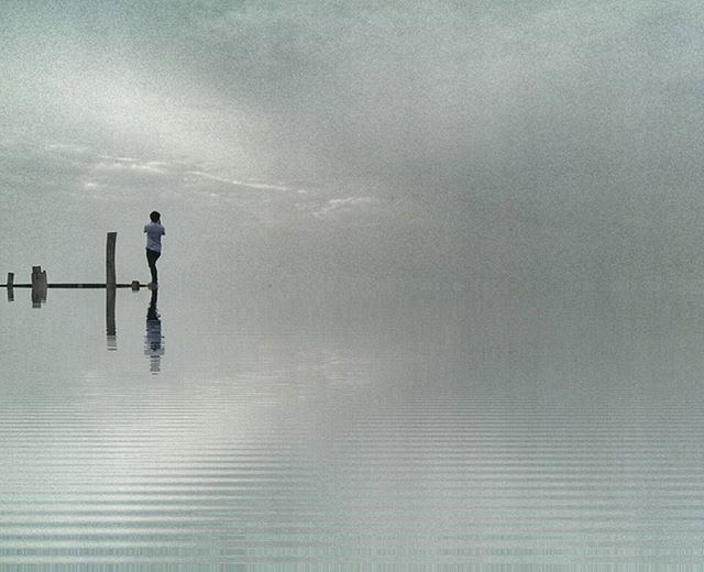 water, sky, sea, waterfront, horizon over water, one person, weather, cloud - sky, reflection, nature, tranquility, day, outdoors, tranquil scene, scenics, full length, beauty in nature, cloudy, dusk, wet