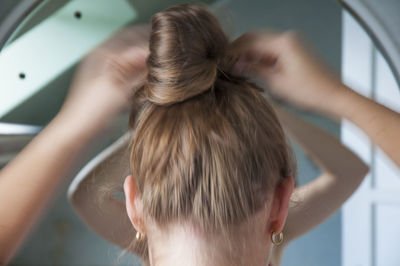 Rear view of woman tying hair while standing at home