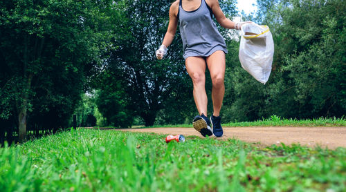 Low section of woman running while holding plastic bag on grass