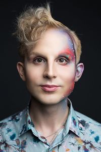 Portrait of young man with make-up against black background