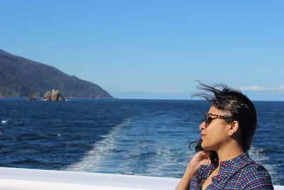 Sideview of a woman wearing sunglasss holding her hair against deep blue doughtful sound