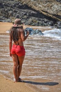 Rear view of woman in bikini standing at beach