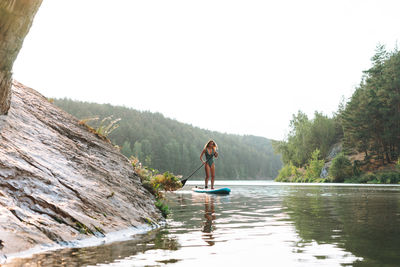 The young woman in green sweemsuit on sup boat with oar floating on river, weekend trip and travel