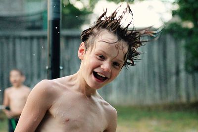 Close-up portrait of shirtless wet boy with tousled hair in backyard