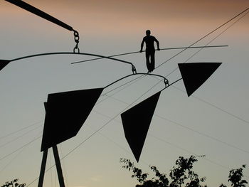 Silhouette person walking on rope against sky during sunset